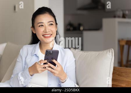 Felice giovane donna asiatica che usa il cellulare a casa Foto Stock