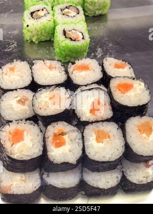 Un vivace assortimento di sushi roll disposti ordinatamente su una superficie riflettente. Sono visibili ripieni colorati, che mostrano ingredienti freschi che invitano Foto Stock