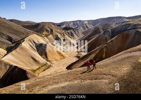 Fai un'escursione di coppia in un paesaggio montuoso mozzafiato, accidentato e colorato di Landmannalaugar in Islanda, che presenta formazioni geologiche con un cielo vivace Foto Stock