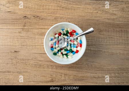 Una ciotola bianca piena di capsule colorate e un cucchiaio. Concetto medico e sanitario. Foto Stock