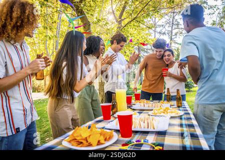 Una coppia che condivide notizie positive con i loro amici multietnici alla festa in un parco Foto Stock