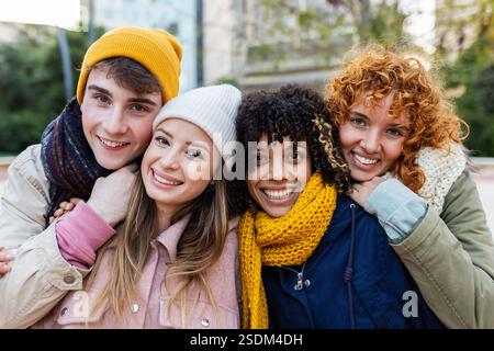 Giovani gruppi di persone diverse che sorridono alla macchina fotografica in piedi all'aperto in inverno Foto Stock
