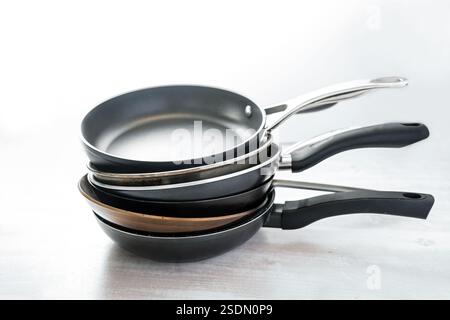 Pila di padelle in ghisa, acciaio al carbonio, rivestimento antiaderente e acciaio inossidabile, per scegliere gli utensili da cucina giusti, dorso grigio chiaro Foto Stock