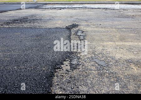 Primo piano di una superficie di asfalto irregolare, che mostra consistenza e contrasto tra materiale vecchio e nuovo Foto Stock