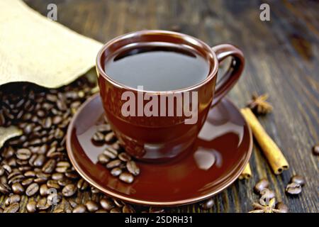 Caffè in tazza marrone con zucchero, un sacco di caffè in grani, bastoncini di cannella e anice stellato su tavole di legno sfondo Foto Stock