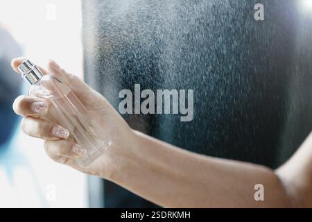 Spruzzare a mano il profumo da una bottiglia di vetro, creando una nebbia profumata Foto Stock