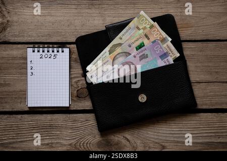 2025 e 123 sono scritti in un quaderno e hrivnia Ucraina in un portafoglio, che si trova su un tavolo di legno, piani per il nuovo anno Foto Stock