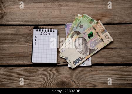 2025 e 123 sono scritti in un quaderno e hrivnia Ucraina, che si trova su un tavolo di legno, i piani per il nuovo anno, scrivono i piani Foto Stock