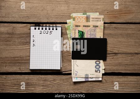 2025 e 123 scritti in un quaderno e hrivnia Ucraina e una carta di credito stesa su un tavolo di legno, piani per il nuovo anno Foto Stock