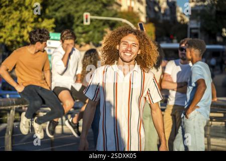 Ritratto di un giovane sorridente con capelli ricci e amici in città al tramonto Foto Stock