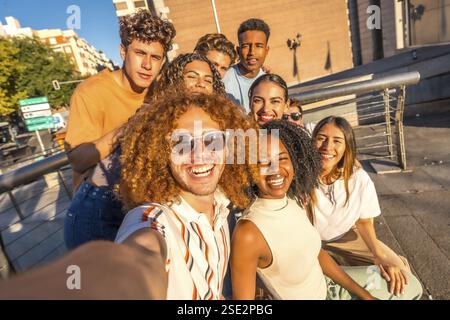 Uomo con capelli ricci e amici multietnici che si fanno selfie in città Foto Stock