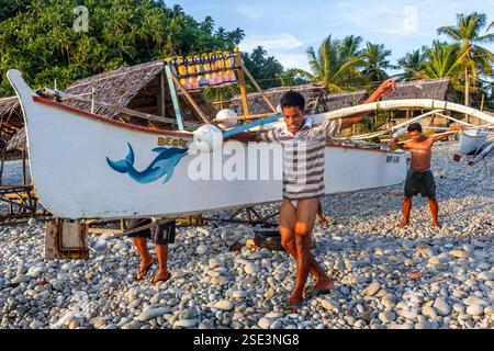 Gruppo di pescatori filippini che praticano il bayanihan, trasportando una banca dalla riva al mare a Surigao nelle Filippine Foto Stock