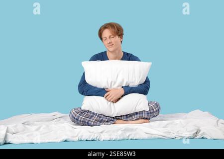 Bel giovane uomo felice in pigiama con cuscino e coperta che dorme su sfondo blu Foto Stock