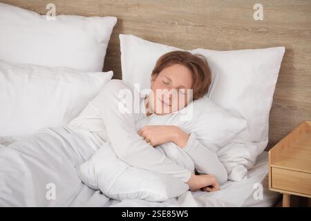Bel giovane uomo felice in pigiama con cuscini che dormono sul letto a casa Foto Stock