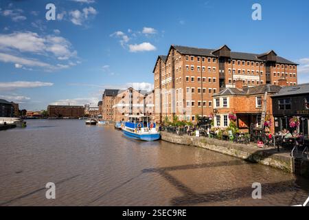 La gente beve in un pub sulle banchine rigenerate di Gloucester Docks, sotto i magazzini vittoriani in mattoni ora convertiti in uso misto residenziale, offic Foto Stock