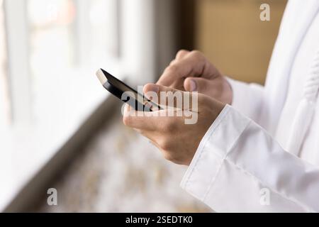 Primo piano colpo ritagliato maschio arabo in Dishdasha utilizzando lo smartphone Foto Stock