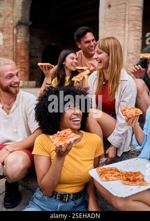 Amici multietnici felici che mangiano pizza all'aperto in un ambiente urbano Foto Stock