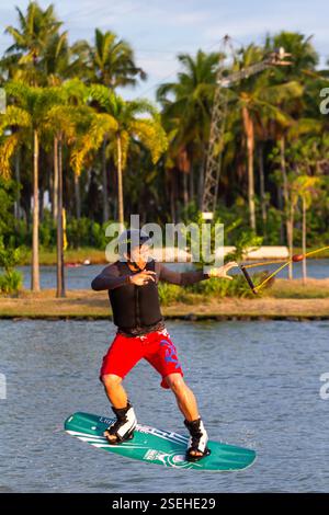Un giovane adulto maschio wakeboarding a tutta velocità in un parco di wakeboard a Davao City, Filippine, catturato a metà azione Foto Stock