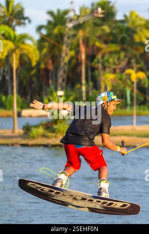 Un giovane adulto maschio wakeboarding a tutta velocità in un parco di wakeboard a Davao City, Filippine, catturato a metà azione Foto Stock