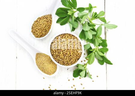 Fieno greco i semi in una ciotola e cucchiaio, massa spice in un cucchiaio con foglie di colore verde sul pannello di legno sfondo da sopra Foto Stock