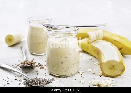 Frullato con semi di chia, semi di lino, farinata d'avena, riso soffiato e banana in due vasi di vetro su uno sfondo di granito Foto Stock