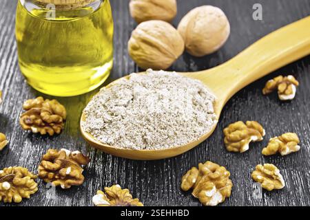 Farina di noce in un cucchiaio, noci sul tavolo e olio in un vaso di vetro sullo sfondo di legno scuro Foto Stock