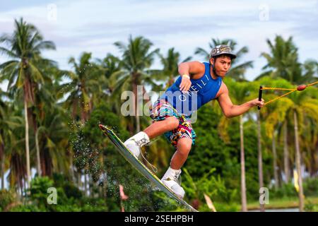 Un giovane adulto maschio wakeboarding a tutta velocità in un parco di wakeboard a Davao City, Filippine, catturato a metà azione Foto Stock