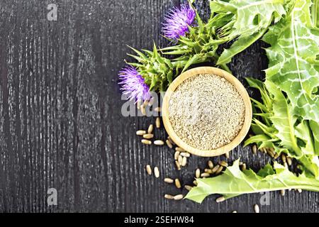 Farina di cardo di latte nel recipiente, semi nel cucchiaio, fiori e foglie di pianta su sfondo di legno dall'alto Foto Stock