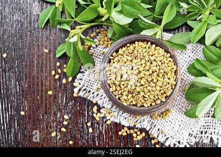 Fieno greco i semi in una ciotola su tela con foglie verdi su una tavola di legno del fondo da sopra Foto Stock