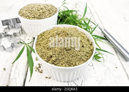 E di farina di grano di canapa in bianco bocce, mixer e cookie cutter, foglie di cannabis sullo sfondo della luce di tavole di legno Foto Stock