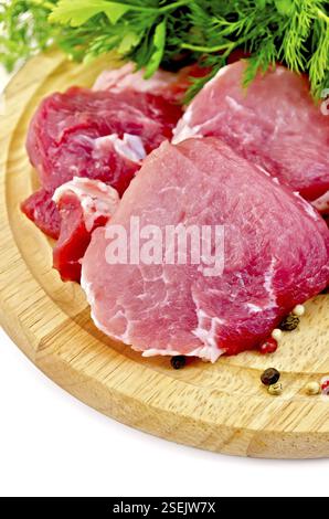 Pezzi di carne, prezzemolo e aneto su una tavola rotonda di legno su sfondo bianco Foto Stock
