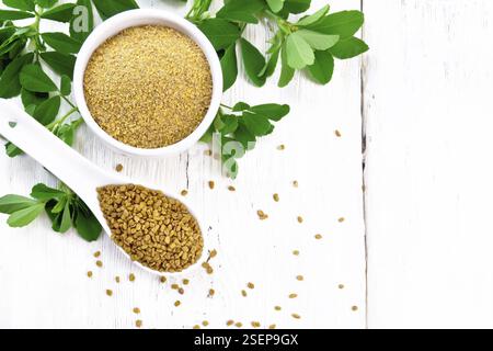 Fieno greco semi in un cucchiaio e la massa spice in una terrina con foglie di colore verde sul pannello di legno sfondo da sopra Foto Stock