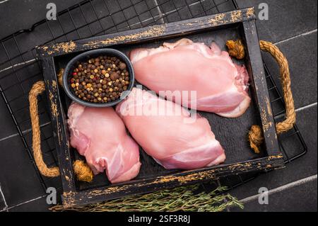 Filetti di cosce di pollo crude in un vassoio di legno fondo nero. vista dall'alto. Foto Stock