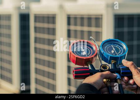 Meccanico addetto alla riparazione dell'aria che utilizza apparecchiature di misurazione per il riempimento dei condizionatori d'aria per impianti industriali e il controllo dell'unità compressore d'aria esterna per la manutenzione. Foto Stock