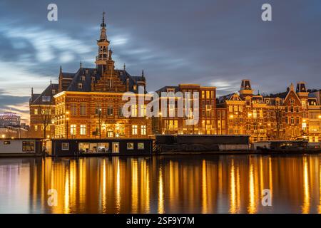 Amsterdam in serata, case galleggianti ed edifici storici si specchiano nel fiume Amstel dopo il tramonto Foto Stock