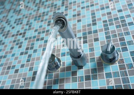 L'acqua corrente del miscelatore del bagno è vista dal basso in un bagno in Inghilterra con pareti piastrellate. Concetto: OFWAT, bollette dell'acqua, utilizzo dell'acqua, spreco di acqua, perdita Foto Stock
