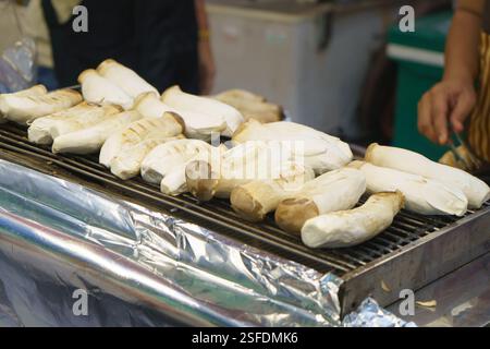 primo piano di grandi funghi di ostriche king grigliati su un barbecue caldo in un vivace chiosco di cibo di strada. La loro consistenza morbida e sostanziosa e saporita Foto Stock