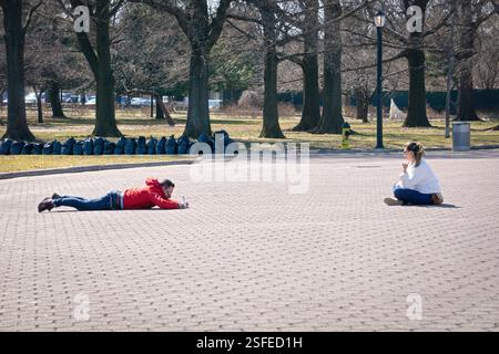 In un deserto Flushing Meadows Corona Park nel Queens, un uomo si mette sulla pancia per scattare una foto al cellulare di una donna della sua vita. Nel Queens, New York. Foto Stock