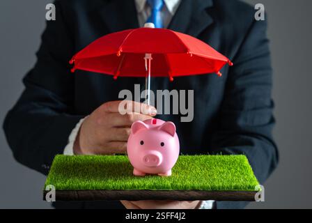 L'uomo d'affari protegge il salvadanaio con un ombrello rosso. Assicurazione sui risparmi. Gestione del rischio, copertura assicurativa, sicurezza degli investimenti, conservazione del patrimonio, e. Foto Stock