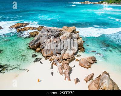 Una vista aerea cattura una donna in un abito giallo in piedi sulla spiaggia di sabbia bianca di la Digue, Seychelles Foto Stock