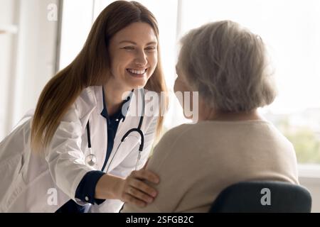Una giovane donna sorridente medico tiene la mano sulla spalla di una donna anziana Foto Stock