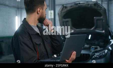 Serio concentrato Caucasico uomo Guy tecnico meccanico auto ingegnere controllare riparazione problema auto diagnostica computer motore elettrico automobile con Foto Stock