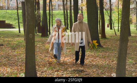 Caucasico felice coppia che cammina insieme con le foglie in autunno parco della città anziani donna matura uomo famiglia passeggiata romantica dattera nella foresta Foto Stock