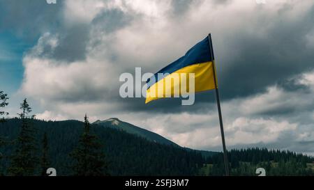 La bandiera Ucraina ondeggia orgogliosamente sullo sfondo di montagne boscose e cieli spettacolari. Foto Stock
