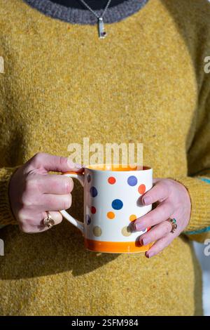 Bristol, Regno Unito. Una donna che tiene in mano una tazza grande di tè o caffè. La tazza calda pesante è supportata da entrambe le mani Foto Stock