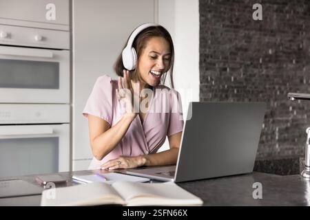Una bella studentessa indossa le cuffie per iniziare una videochiamata sul laptop Foto Stock