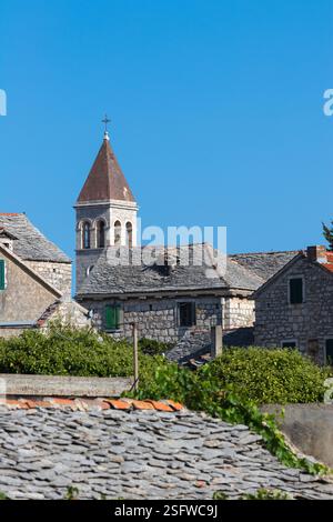 Un pittoresco villaggio caratterizzato da tradizionali edifici in pietra e da un'importante torre della chiesa, adagiata su un cielo azzurro. Foto Stock