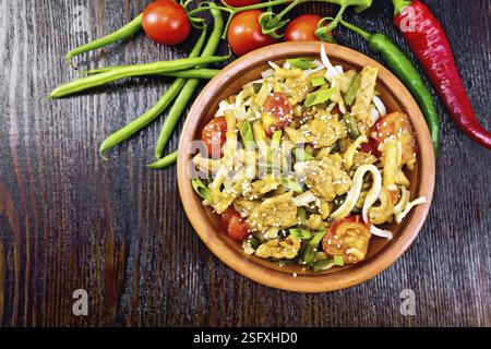 Tagliatelle thailandese wok con carne di pollo, pomodori, la salsa di soia e i fagiolini verdi cosparsi con i semi di sesamo in una piastra sullo sfondo di una tavola di legno fro Foto Stock
