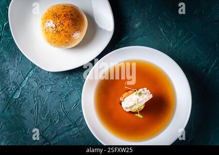 Zuppa o consomme, brodo di carne denso con carote, gnocchi di pollo serviti in un piatto bianco su sfondo verde scuro con panini di sesamo, tovagliolo Foto Stock