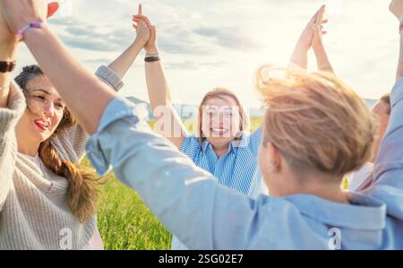 Ritratto di quattro allegre donne sorridenti e ridenti che si tengono mano in mano e IN SU durante il tramonto camminando lungo la verde collina. Un'amica di donna Foto Stock